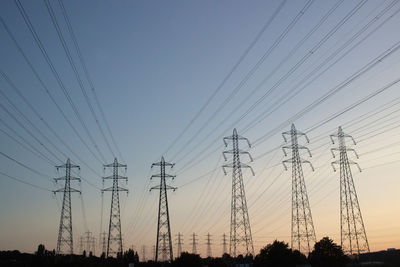 Low angle view of electricity pylon against sky at sunset