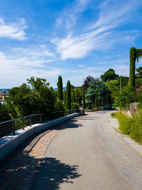 Empty road along plants and trees against sky