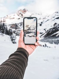 Cropped hand of person photographing snowcapped mountain with smart phone