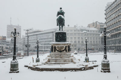 Statue in city against sky during winter