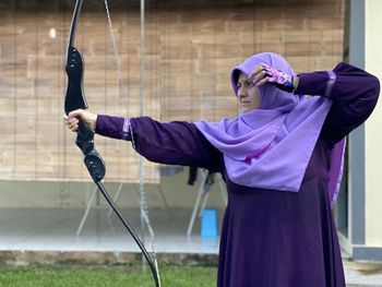 Rear view of woman standing against wall doing archery