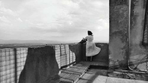 Rear view of woman standing on railing against sky