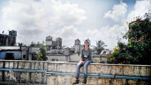 Woman sitting on railing against sky in city