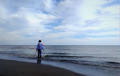 Rear view of man standing on beach against sky