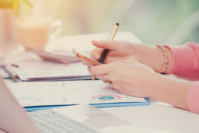 Cropped hands of woman using mobile phone on table