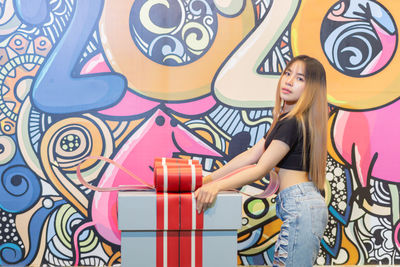 Full length of a smiling young woman standing against graffiti wall