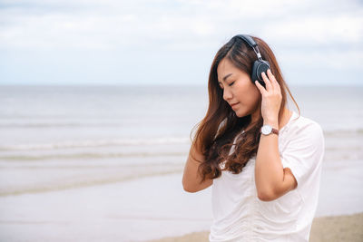 Woman listening to music while standing at beach