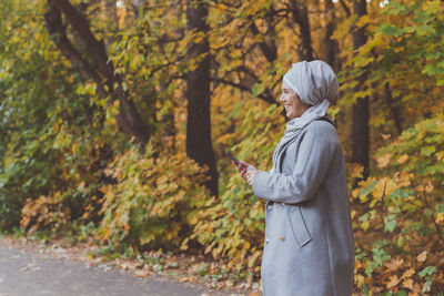 Side view of woman standing by tree during autumn