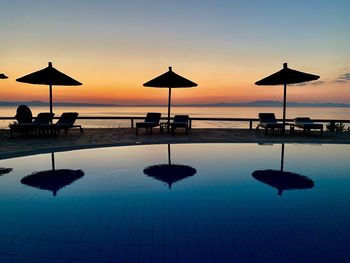 Silhouette swimming pool by sea against sky during sunset