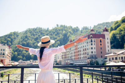 Woman with arms outstretched standing against built structure