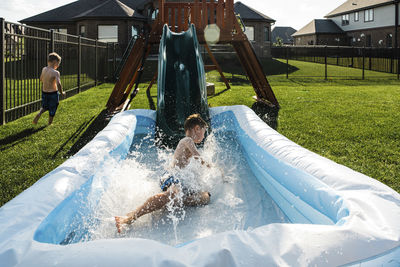 Brothers sliding into wading pool at park