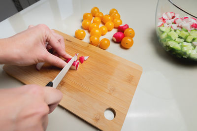 Close-up of female hands cut fresh raw radish on a wooden board against the background of yellow