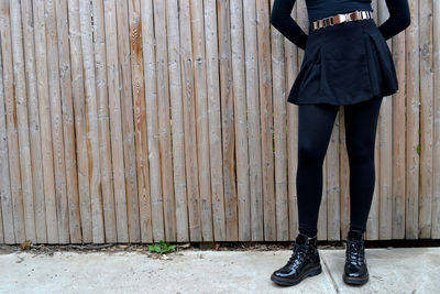 Low section of woman standing on sidewalk while leaning on wooden fence