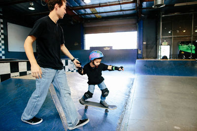 Skateboard instructor holds hands alongside student on skateboard