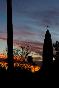 Silhouette church in front of tower against sky during sunset