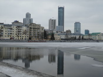 Reflection of buildings in lake against sky in city