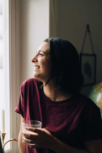 Thoughtful smiling woman having tea while looking through window