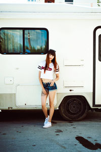 Full length portrait of young woman standing by camper trailer on street