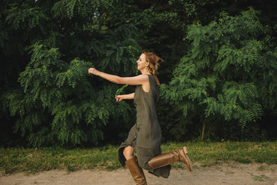 Woman runs on a dirt road near the trees in a dress and boots