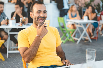 Cheerful man smoking cigar while sitting at outdoor restaurant