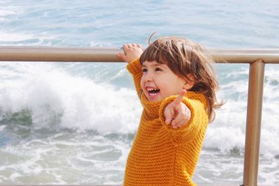 Cheerful girl pointing while standing against sea