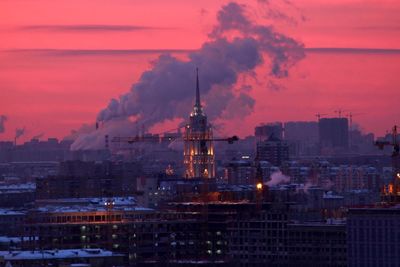 Illuminated buildings in city against sky at sunset