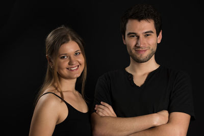 Portrait of smiling young couple against black background