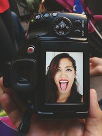 Cropped image of hand holding camera with woman sticking out tongue on screen