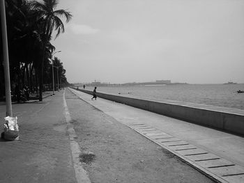 Man on footpath by sea against sky