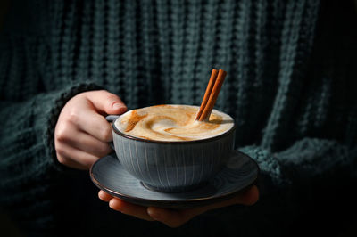 Woman holding cup of cappuccino with cinnamon sticks