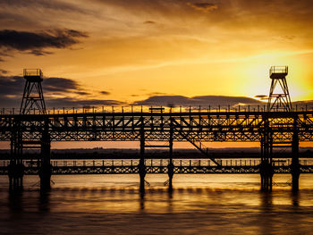 Silhouette bridge over sea against sky during sunset