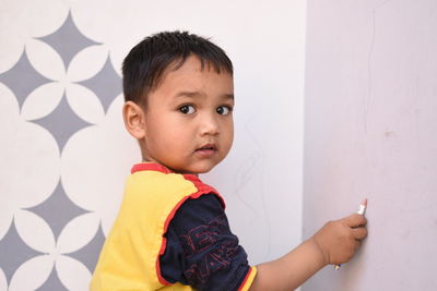 Portrait of boy writing on wall with pencil