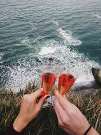 Cropped hands of people toasting wine against sea