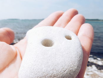 Cropped hand holding pebble at beach on sunny day