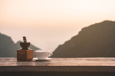 Coffee cup on table against sky during sunset