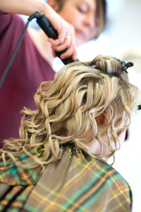 Female hairdresser using equipment on blond bride at salon