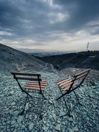 Empty chairs on land against sky