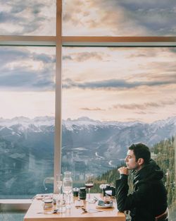 Side view of man sitting against window at restaurant