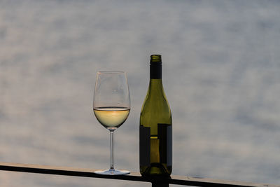 Close-up of bottle and wineglass on railing against sea