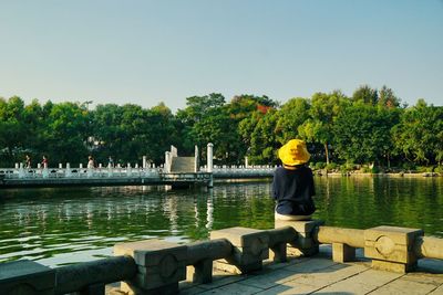 Woman sitting on pier by lake against sky