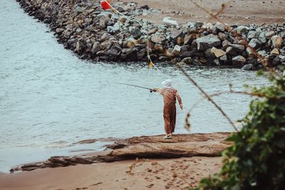 Rear view of fisherman fishing while standing on shore