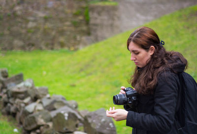 Female hiker holding camera while standing on field