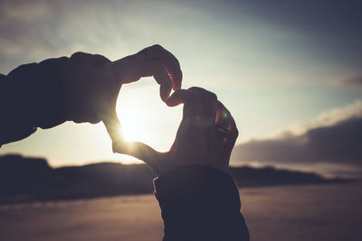 Silhouette man holding heart shape against sky during sunset