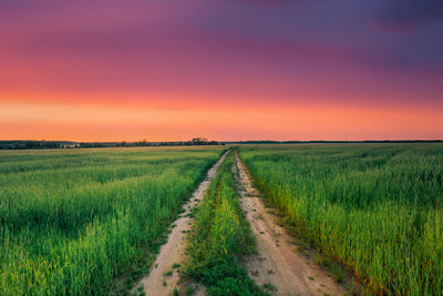 Road amidst field against sky during sunset