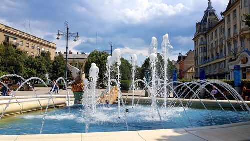 Water fountain in swimming pool against buildings in city