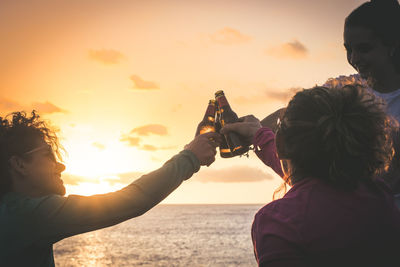 Rear view of man holding woman against sky during sunset