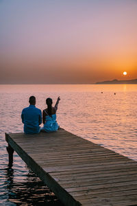 People sitting on sea against sky during sunset