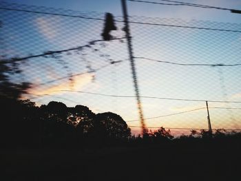 Silhouette trees by fence against sky during sunset