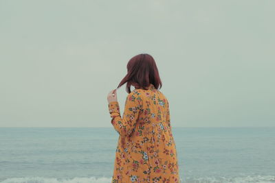 Rear view of woman standing at beach against sky