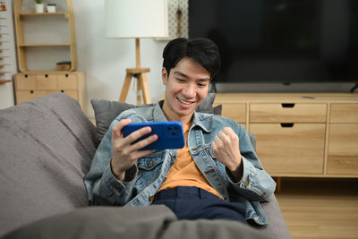 Side view of young woman using mobile phone while sitting on sofa at home
